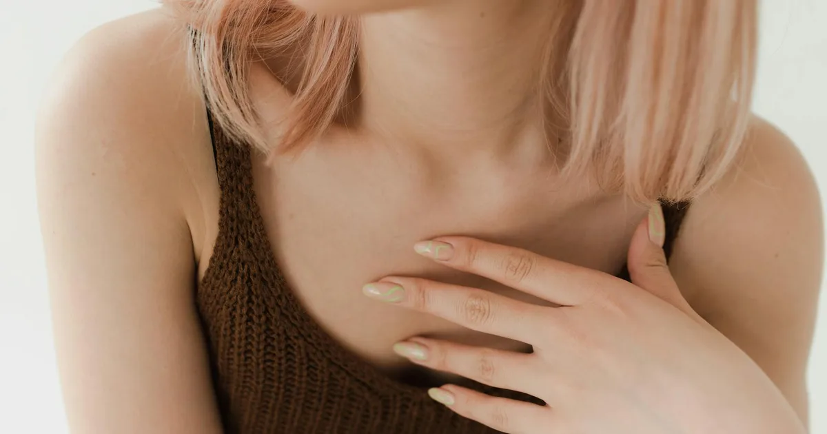 Close-up of a woman's manicured hand on chest in a knitted top. Warm and neutral tones.