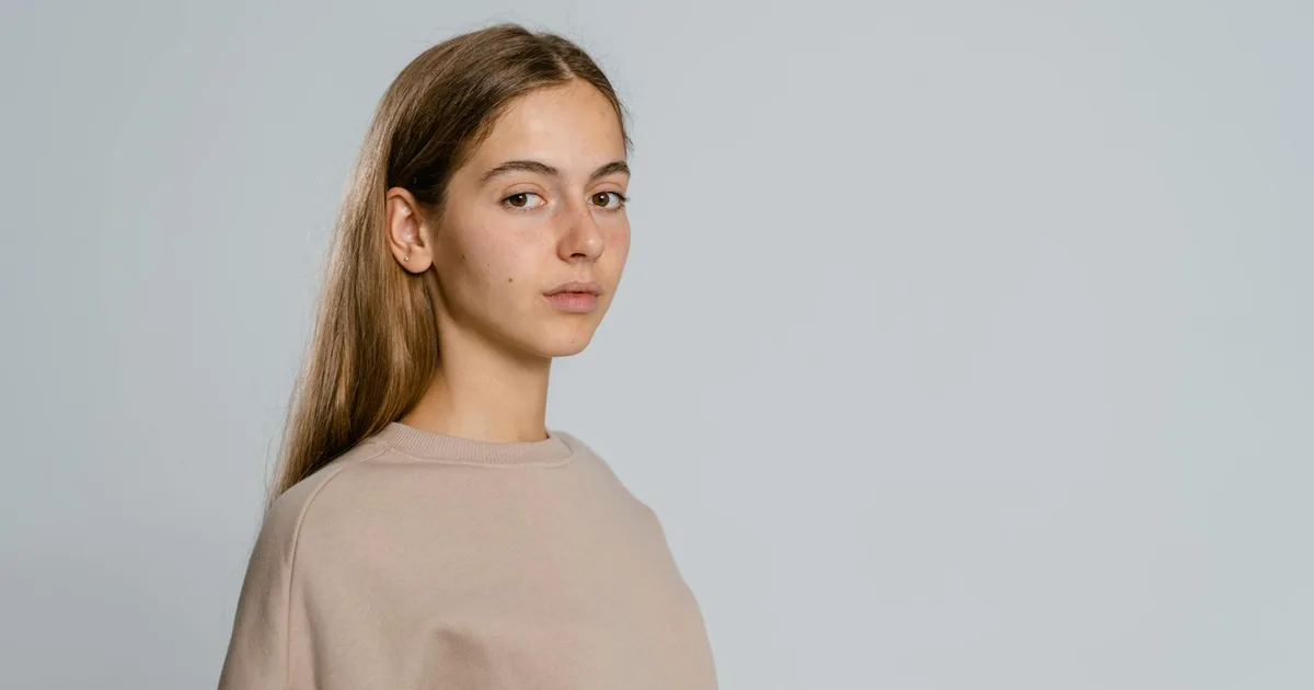 Portrait of a young woman wearing a beige top against a neutral background, perfect for fashion or lifestyle themes.