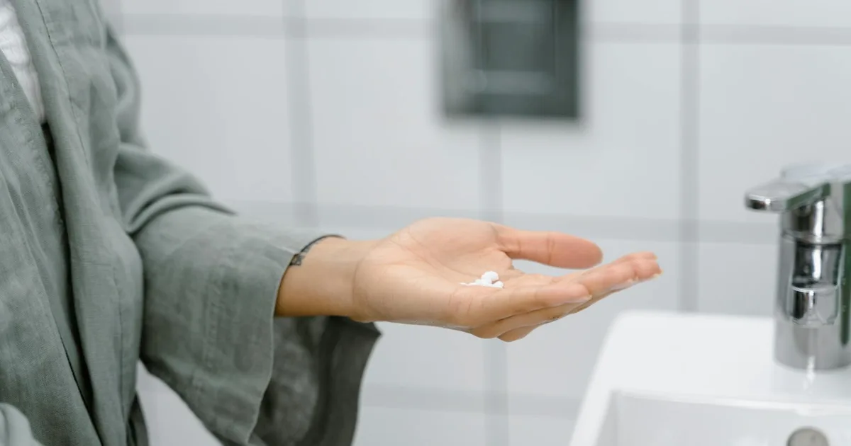 A close-up of a hand holding cream near a modern bathroom sink.