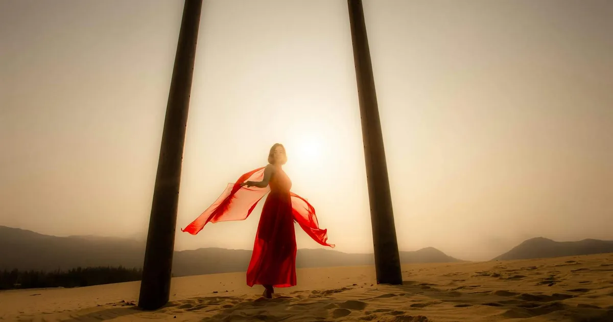 A woman in a red dress poses against a stunning desert sunset, creating an inspiring silhouette.