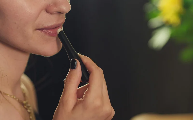Close-up of a woman applying lipstick, featuring a blurred background for a soft focus effect.