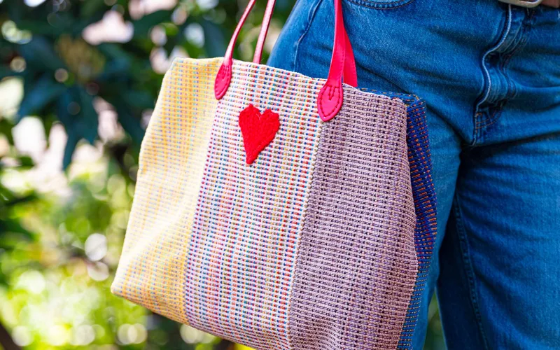 Close-up of a stylish woven tote bag with a heart shape outdoors.