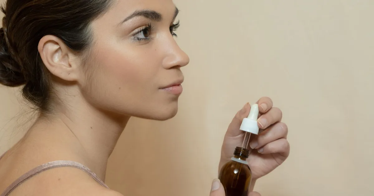 Side profile of a young woman holding a dropper bottle for skincare routine.