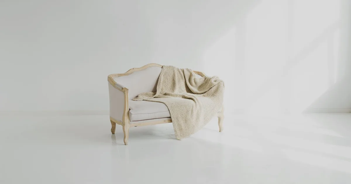 A beige throw on a vintage white sofa in a bright minimalist living space.