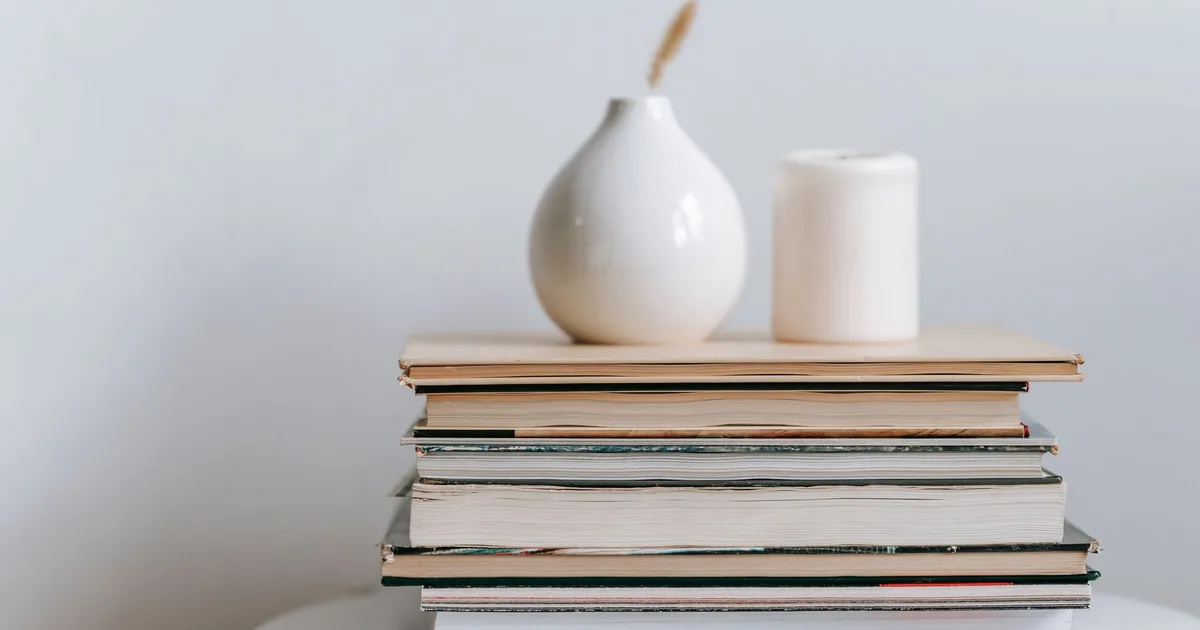 Composition of white vase and candle with pile of books on table on white background