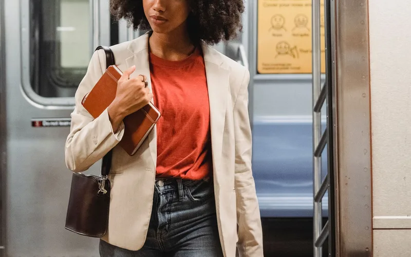 Confident woman in a blazer with notebook and purse walking in a subway train.