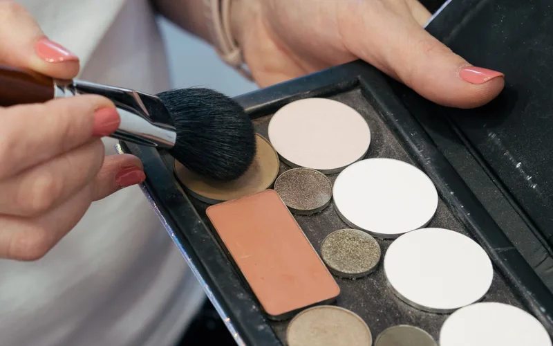 Female hands holding a makeup brush and palette for cosmetic application.