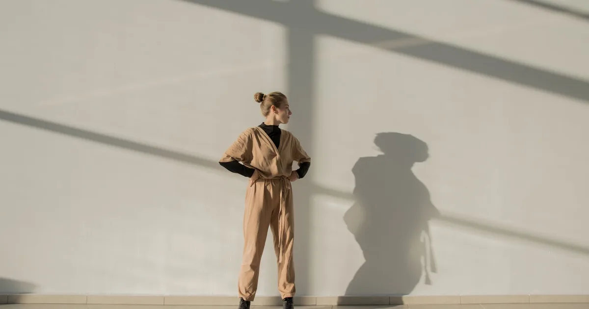 Woman in a beige outfit casting a shadow indoors with sunlit lines.
