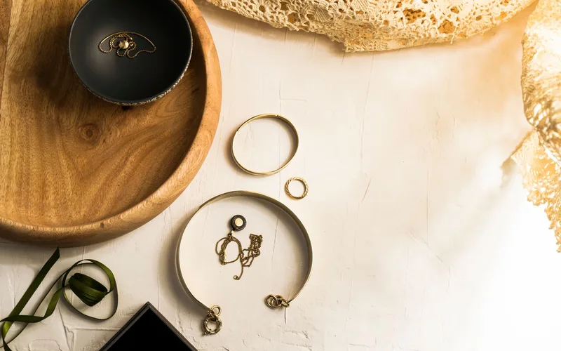 Elegant display of gold jewelry on a wooden tray with top view on a white surface.