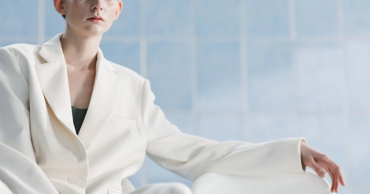 Stylish portrait of a woman in a white suit set against a minimalist blue background.