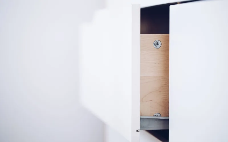 Close-up of an open white drawer revealing a wooden interior and screws in a minimalist design.