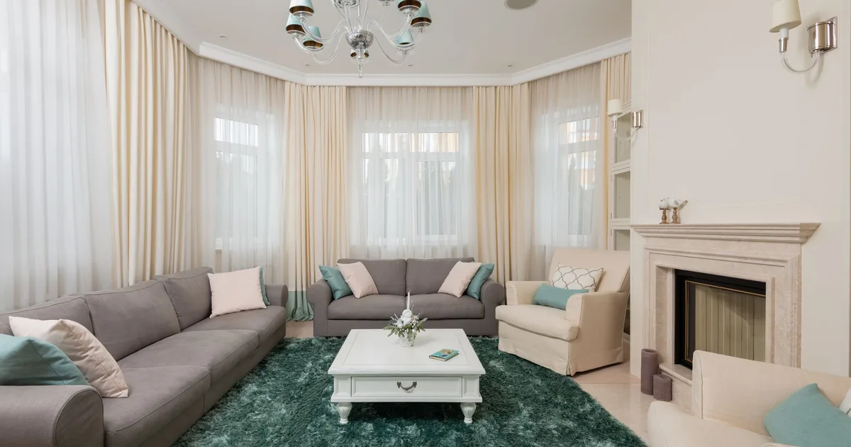 Interior of classic living room with gray sofas and beige armchair on soft carpet near stone fireplace under chandelier