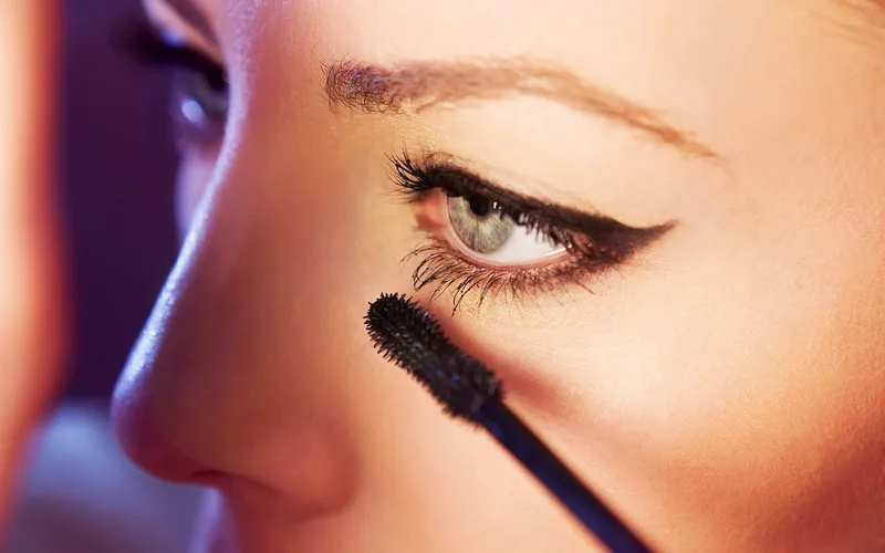 Detailed close-up of a woman applying mascara to her eyelashes, highlighting eye makeup.