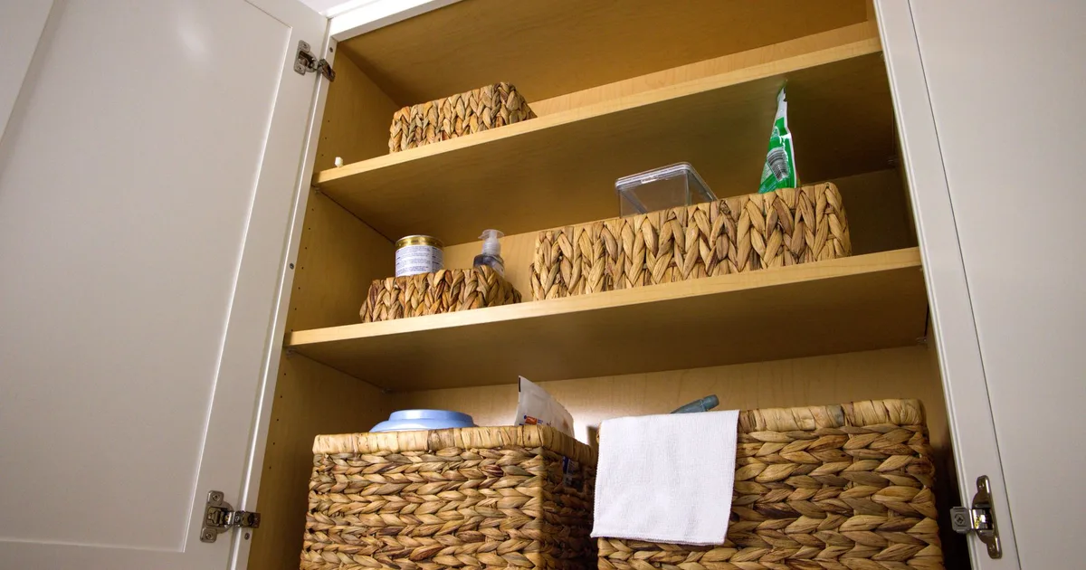 Neat storage in a kitchen cabinet using wicker baskets for a clean aesthetic and organization.