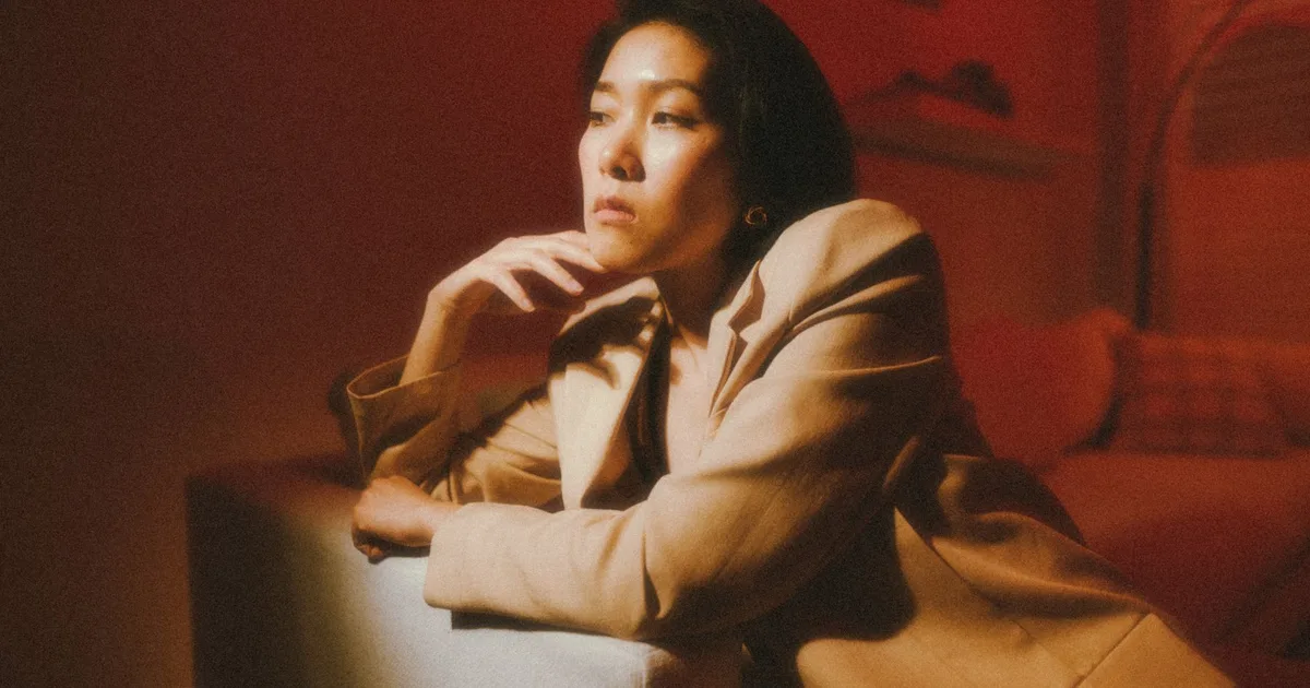 Fashion portrait of a woman in beige suit with red lighting, exuding elegance and contemplation.