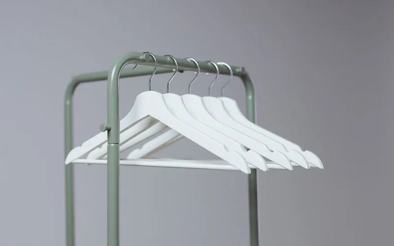 A minimalist indoor clothes rack featuring white hangers with a soft-neutral tone.